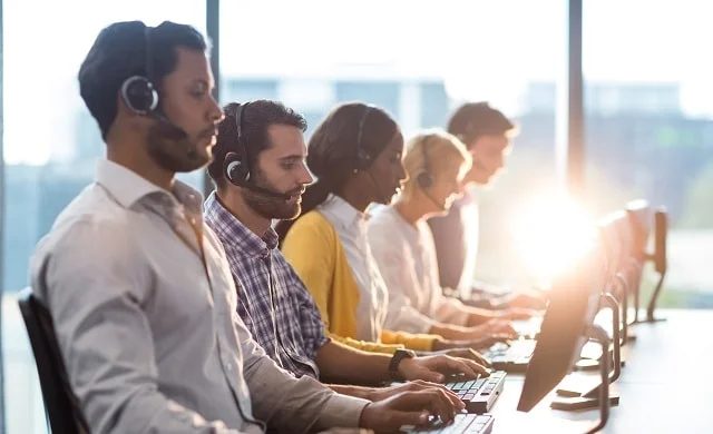 Customer support team wearing headsets working at computers in a bright office